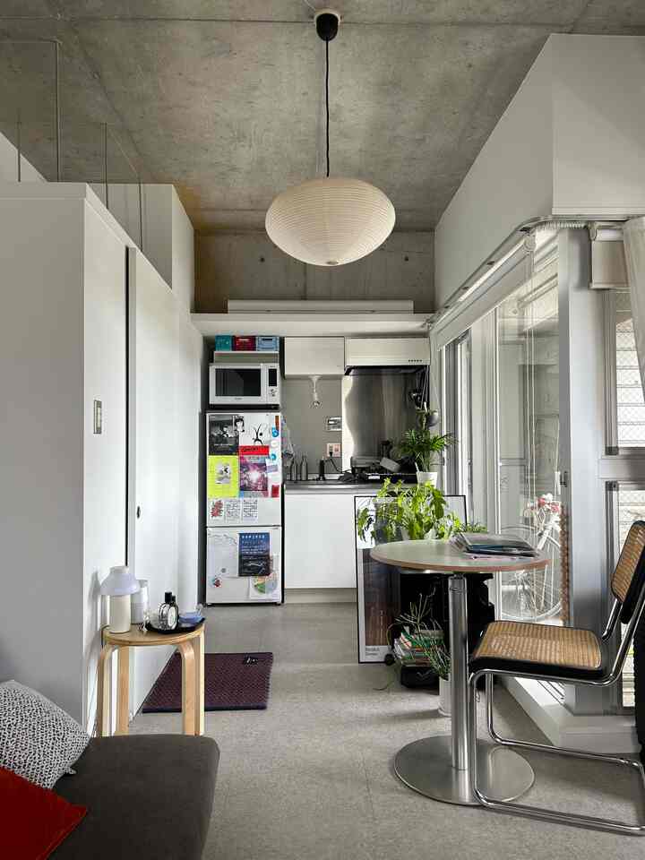Bright white studio apartment kitchen and dining area featuring natural wood furniture near large window with clean and open atmosphere