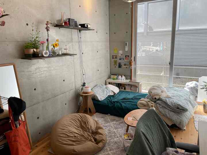 ナチュラルカラーの小さな寝室、ベージュのビーズクッションと大きな窓際に配置された低いベッドがある雰囲気のある空間