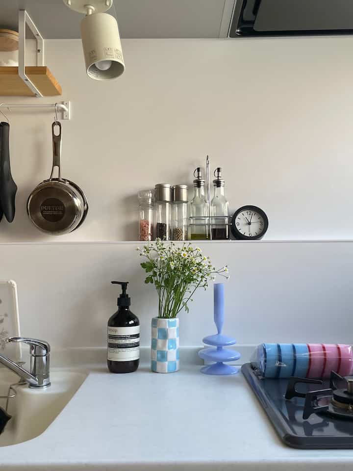 A simple and clean kitchen space with white and natural wood tones, featuring aromatic hand wash and a floral vase