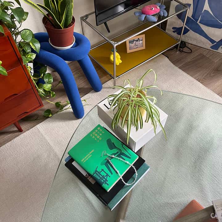 An 8-tatami studio living room with a transparent glass coffee table, multiple green plants, blending Mid-Century Modern and Nordic styles