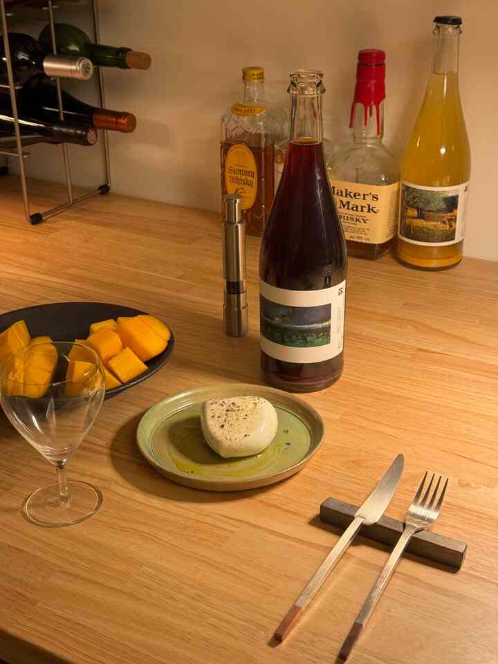 ナチュラルな木目調のキッチンカウンターにワインボトル、ソルト＆ペッパーミル、食器、ワイングラスが配置された印象的な一人暮らしの空間