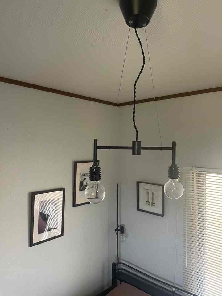 A bedroom with light gray walls and white ceiling, featuring black pendant lights and a floor lamp, showcasing a modern and simple atmosphere