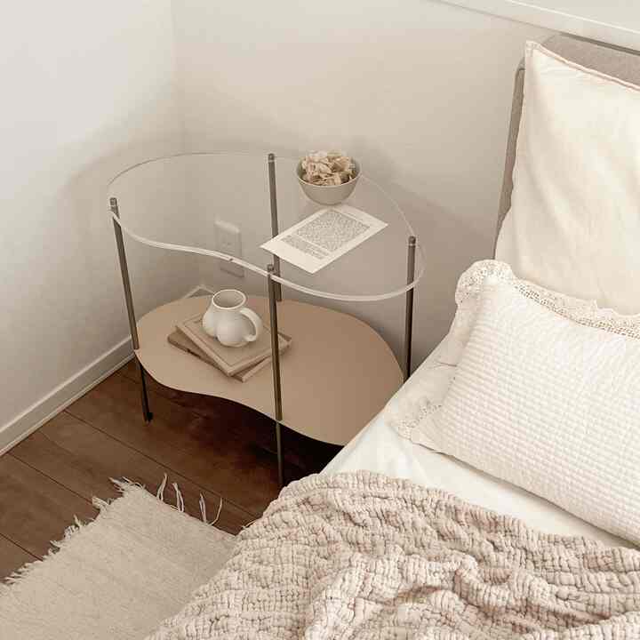 Natural tone bedroom corner in white and brown featuring an acrylic and beige side table with cozy bedding