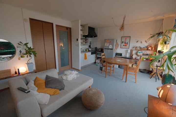 ナチュラルなトーンの1LDKリビングとダイニング、木製のダイニングテーブルとソファ、多数の植物が配置された雰囲気のあるインテリア