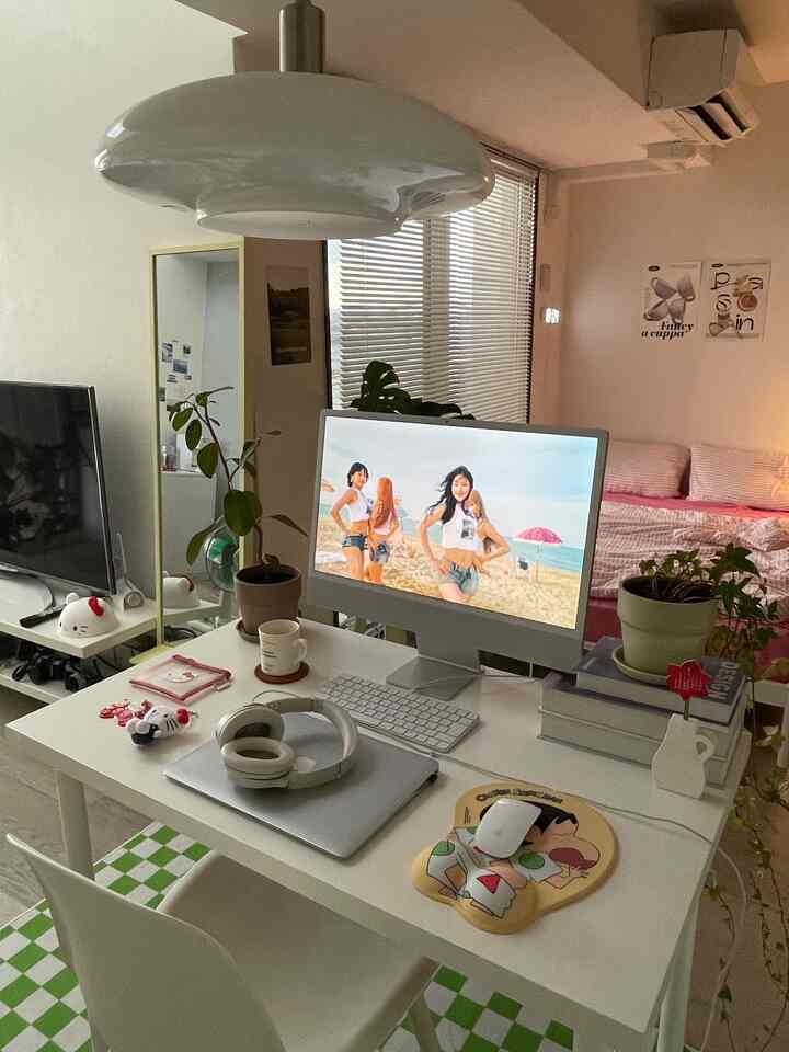 白とピンクのトーンのワンルーム、デスクとコンピューターが配置された居心地良いコンパクトな二人暮らしのインテリア