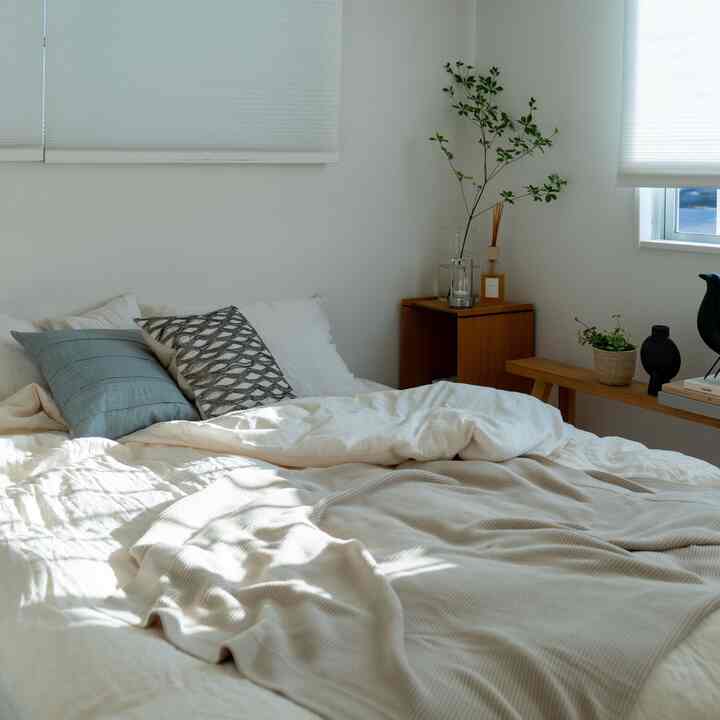 白と木目調が調和した寝室、柔らかな寝具と植物が配置された雰囲気のあるインテリア
