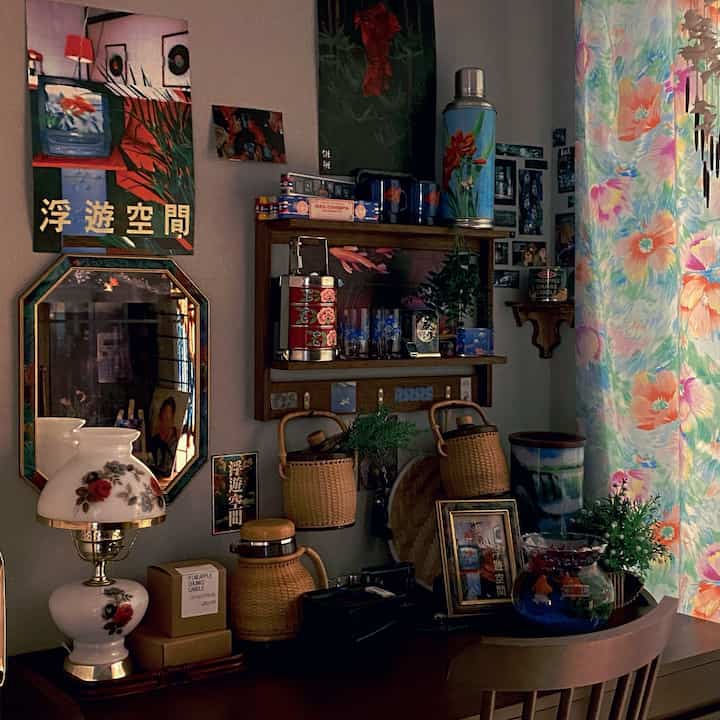 ヴィンテージな木目調の小さな空間、絵額や植物が置かれたテーブルと壁の装飾が調和する雰囲気のあるインテリア