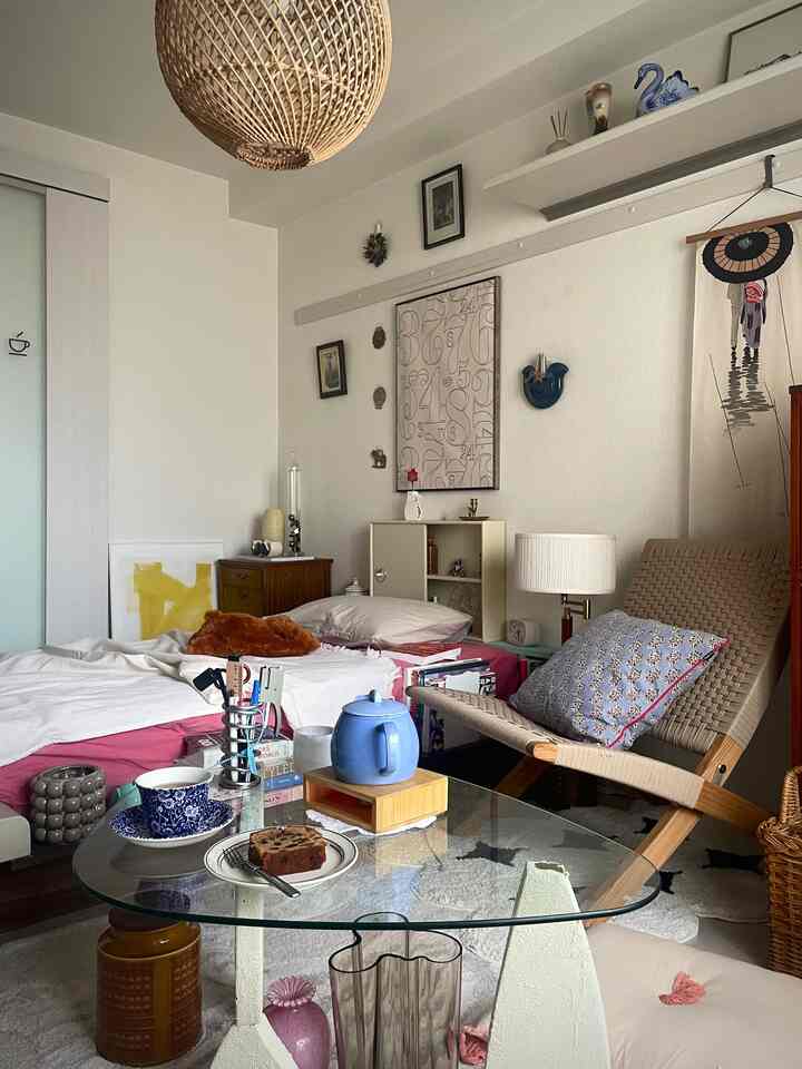 White-walled single household bedroom featuring brown rattan lighting and a lounge chair in home cafe style