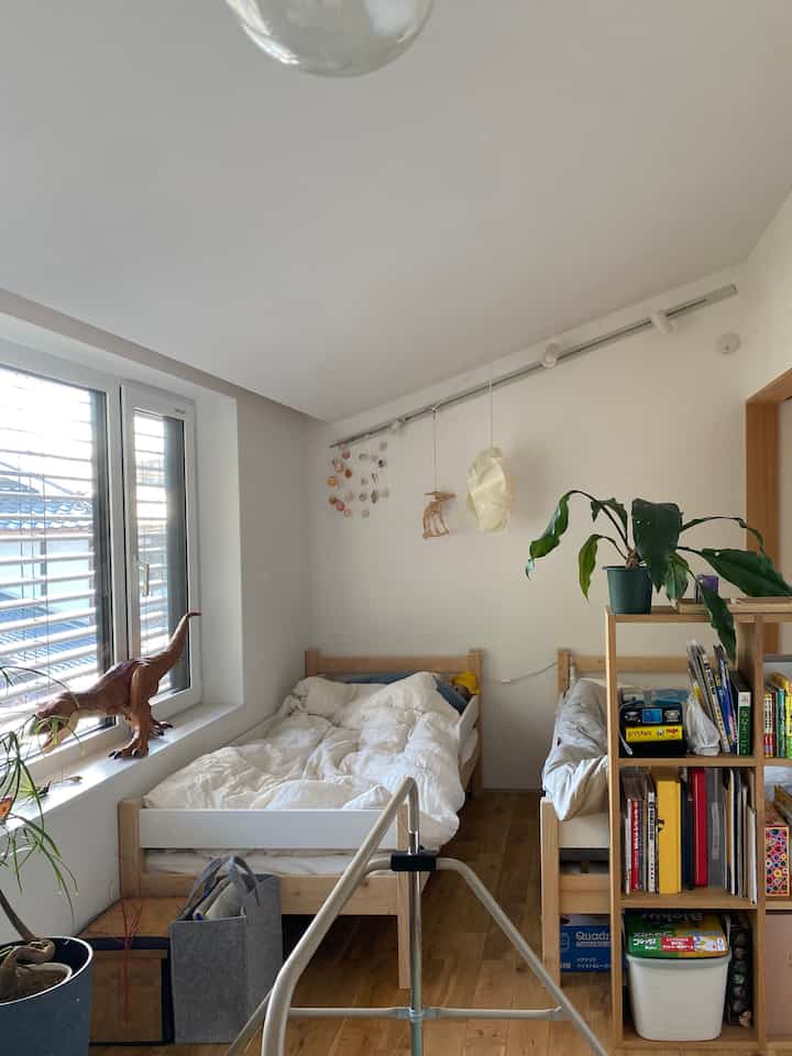 ナチュラルカラーと白を基調としたコンパクトな子供部屋、二台の小さなベッドと本棚が配置された雰囲気のあるインテリア