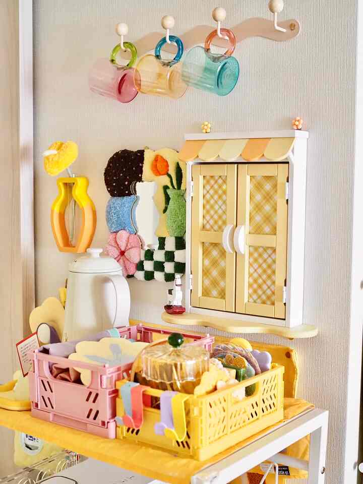 黄色とオレンジのトーンのキッチン、チェック柄のインターフォンカバーとカラフルなカップが配置された雰囲気のあるインテリア