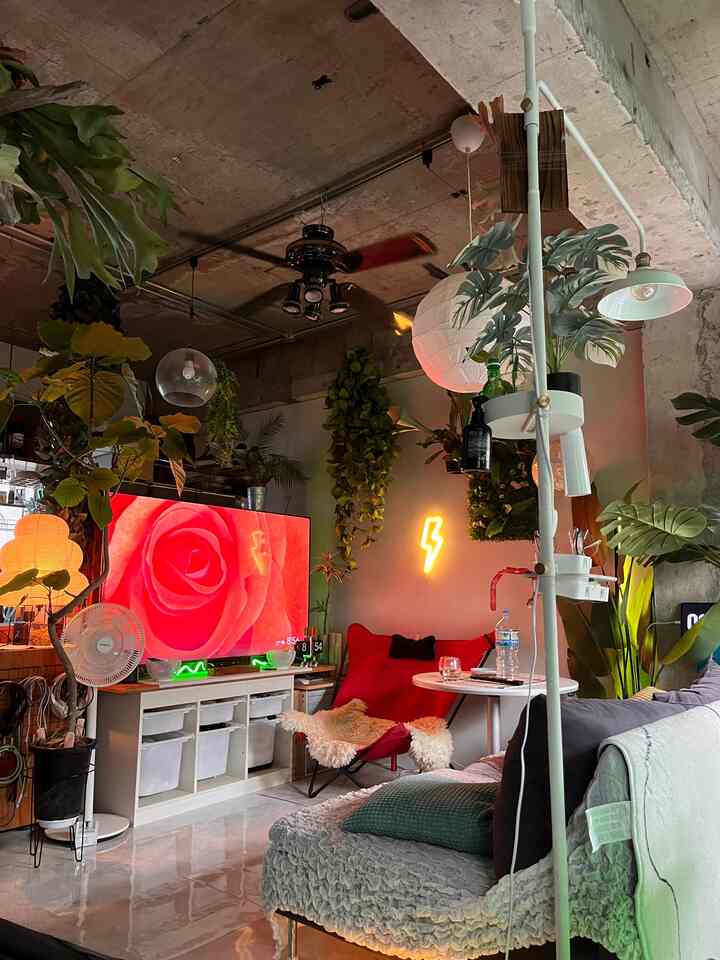 白と緑、赤の色調が調和するワンルームリビング、赤い椅子と豊かな観葉植物、ネオンサインが印象的な空間