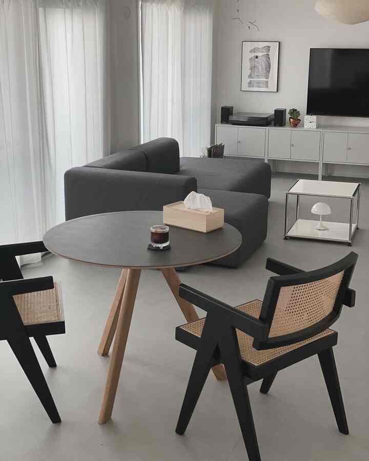 White-toned living room featuring a modern gray sofa, wooden round table, and black rattan chairs creating a simple and natural ambiance
