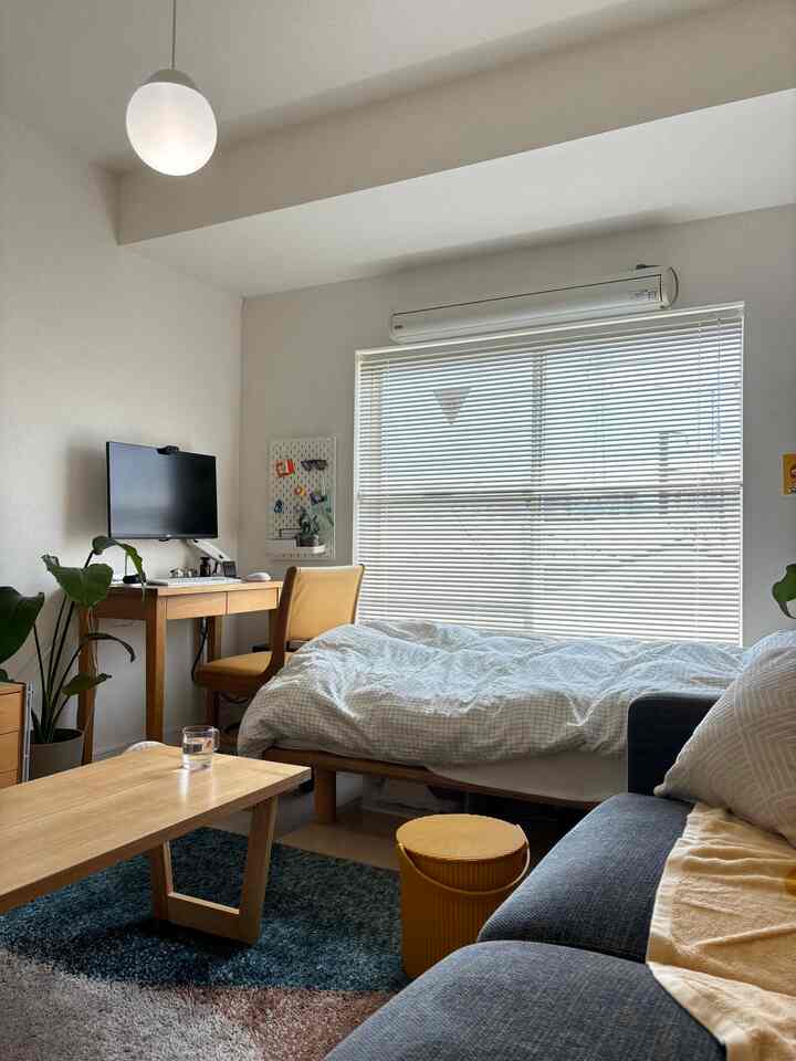 Natural wood tones and white dominate this Nordic-inspired 1K studio apartment for a single household featuring bed, desk, and sofa with cozy ambiance