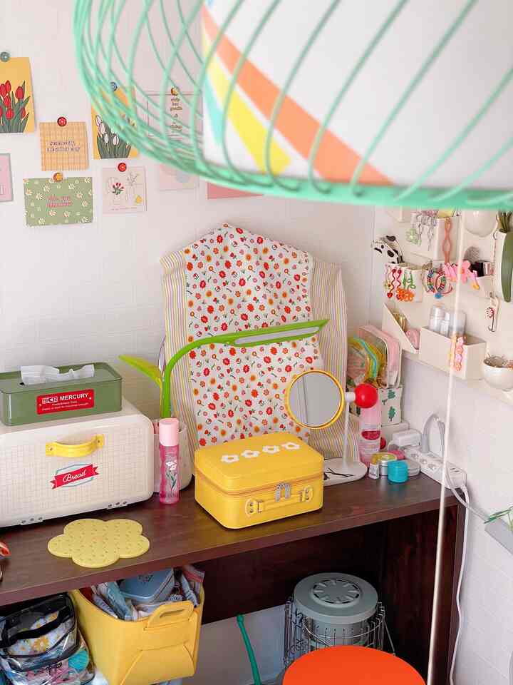 明るく鮮やかなイエローとグリーンのトーンのミッドセンチュリーモダンなメイクスペース、花柄のチェアカバーとカラフルな壁の装飾が印象的な整った化粧台の空間