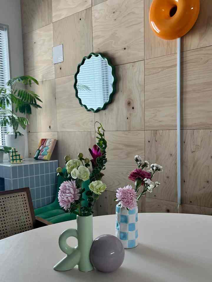 ナチュラルな木製パネル壁と丸テーブルに花瓶や装飾が配置された雰囲気のあるリビング空間