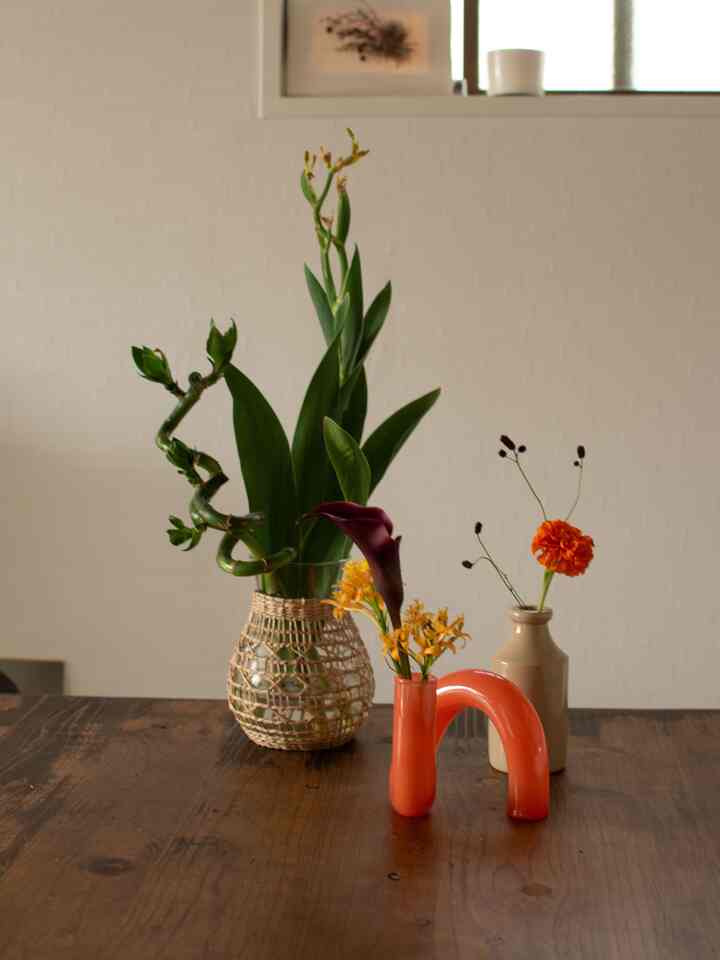 ナチュラルなブラウンの木目調テーブルの上に、多様な色彩の花瓶と花が配置されたシンプルで落ち着いた雰囲気のインテリア