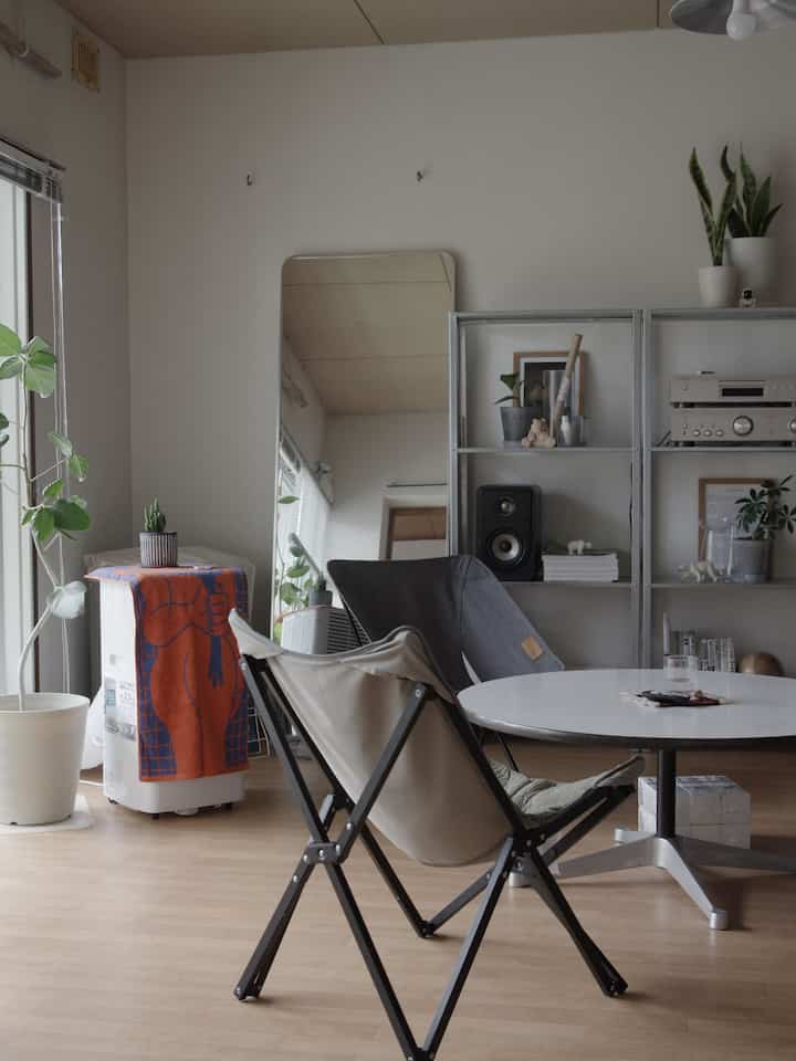 Living room with brown wood flooring and white walls, featuring round table and outdoor chairs in a simple natural style