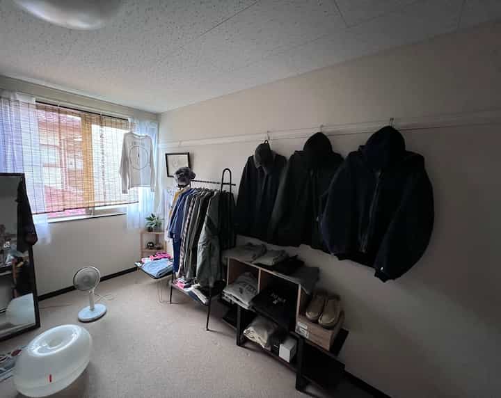 Beige-toned small room featuring a black coat rack on the right wall with neatly arranged clothing