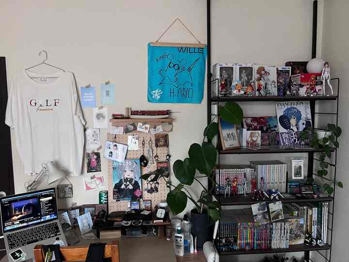 ナチュラルトーンの一人暮らしの部屋、机とモンステラの植物、フィギュアが並んだ本棚が配置された落ち着いた空間