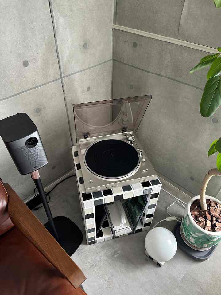 シルバーと黒の色調のモダンなコンクリート壁の空間、サイドテーブルに置かれたレコードプレーヤーと植物が配置された印象的なインテリア