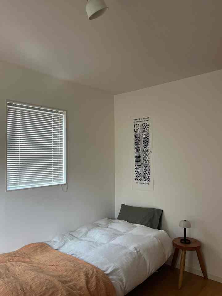 A white and brown toned bedroom featuring a bed with pillow and bedding, wooden nightstand with table lamp, showcasing a simple and modern atmosphere