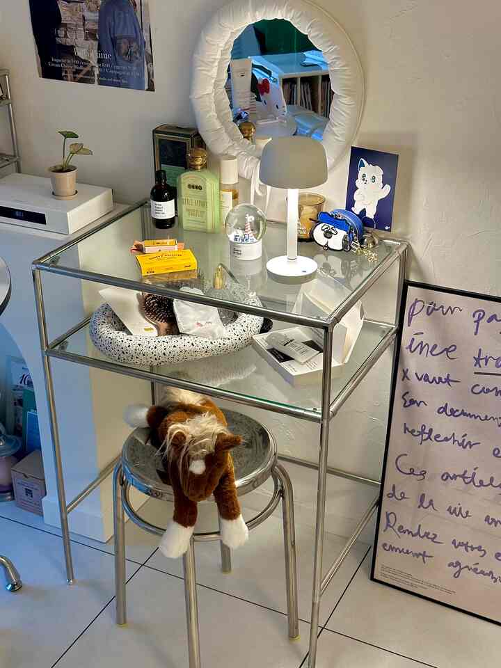 White and silver toned bedroom vanity area featuring a round stool, circular mirror, and table lamp with a cozy ambiance