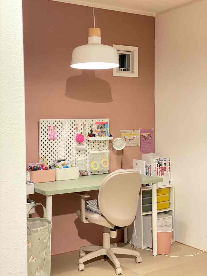 ピンク色のアクセントウォールとナチュラルな色合いの子供部屋、ホワイトのペンダントライトとアイボリーのオフィスチェアが配置された雰囲気のあるインテリア