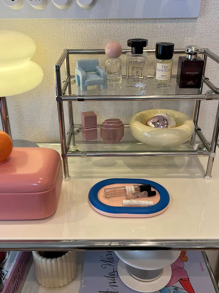 Pink and white toned vanity area with a modular shelf displaying neatly arranged perfume bottles in a clean setting