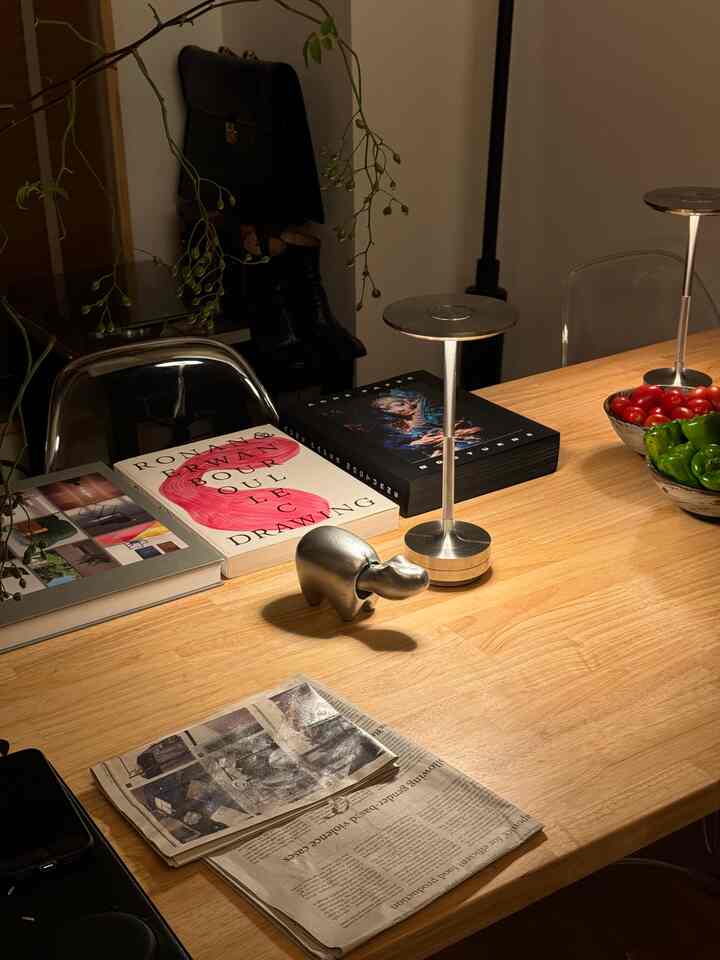 ナチュラルな木目調のダイニングテーブルにシルバー色の小さなオブジェと本が置かれた、温かみのある雰囲気のあるインテリア