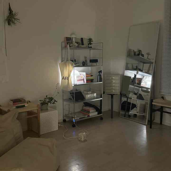 明るい白とナチュラルカラーのリビング、ラタンのウッドスツールとビーンバッグソファ、メタルの棚が配置されたシンプルで落ち着いたインテリア