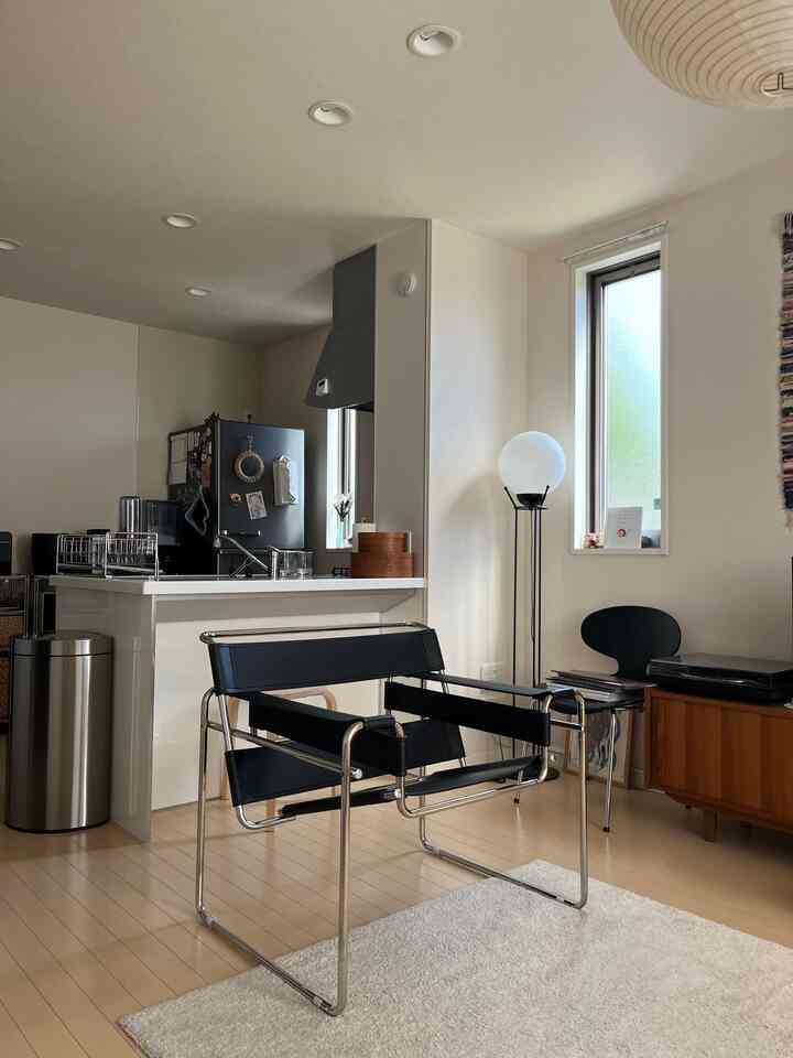 白い壁と木目調の床を持つモダンなリビング、中央にブラックのアールデコスタイルのアームチェアが配置された印象的な空間