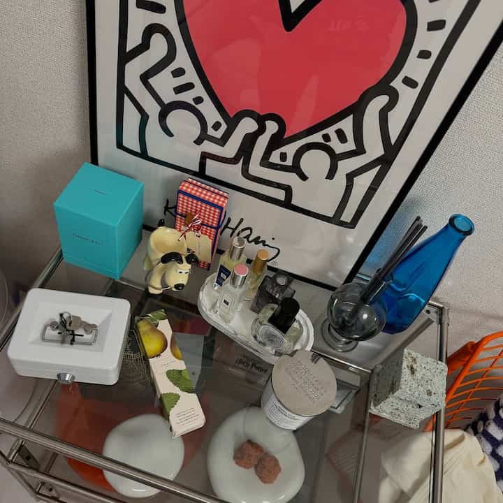 白と透明なガラスのテーブルがある空間、香水や額縁などの多彩な小物が配置された印象的なインテリア