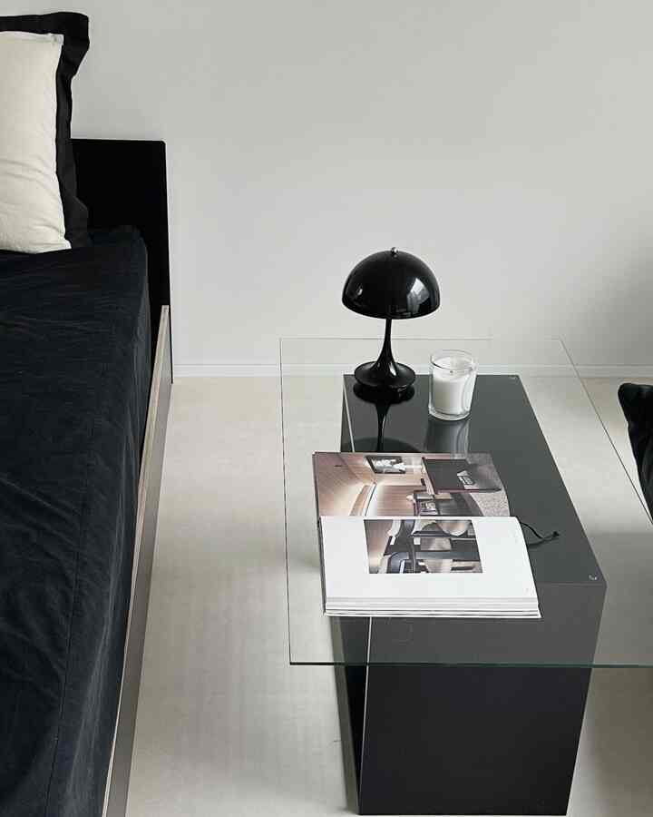 Modern style living room featuring a black sofa bed, glass coffee table, and table lamp creating a simple atmosphere