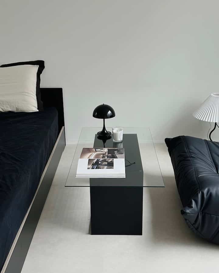 Black and white toned living room featuring a modern armchair and glass-top coffee table with a simple, clean atmosphere
