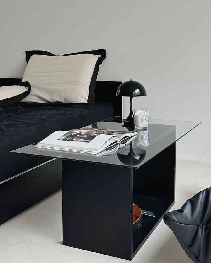 Black and white tone bedroom featuring a black bed, glass nightstand, and a modern minimalist atmosphere