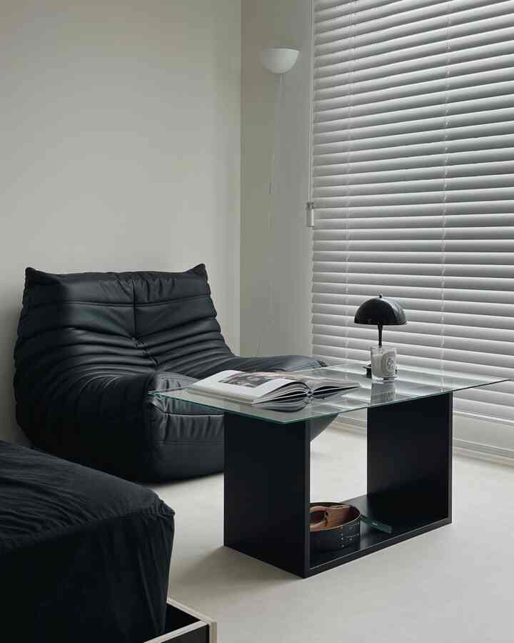 Modern bedroom with black and transparent elements, featuring a mini table and blinds in a clean setting