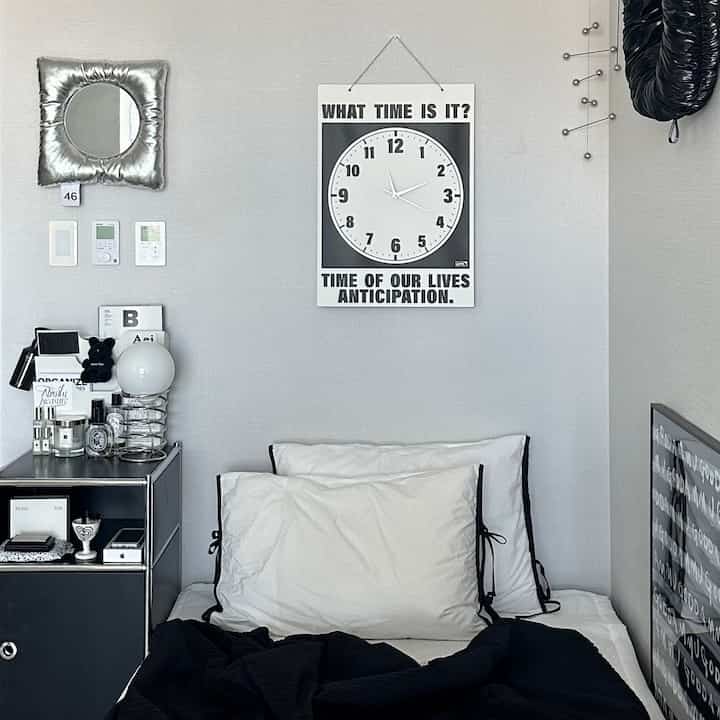 A modern bedroom in white and black tones featuring a large wall clock and neat bedding