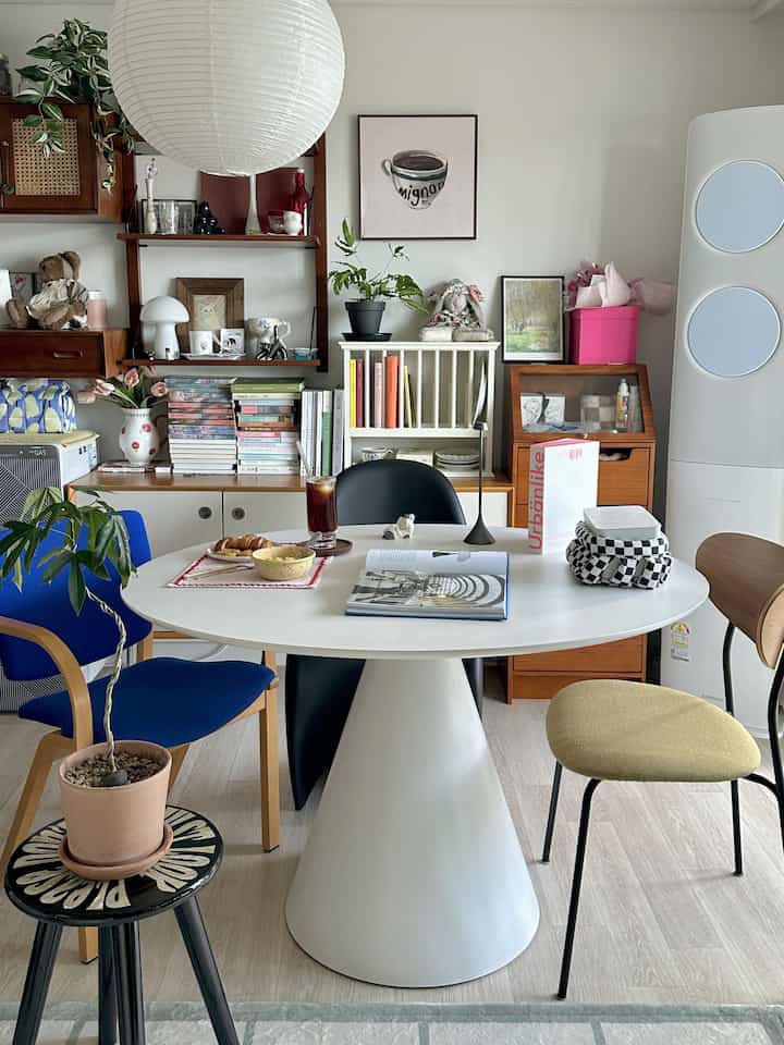 白と青の色調のリビング、円形テーブルとヴィンテージチェア、大型照明と無風エアコンが調和した印象的な空間