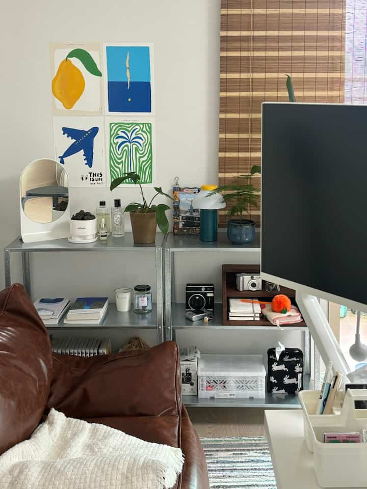 Modern home office space with white walls and brown leather sofa, featuring metal shelves and plants for a cozy atmosphere
