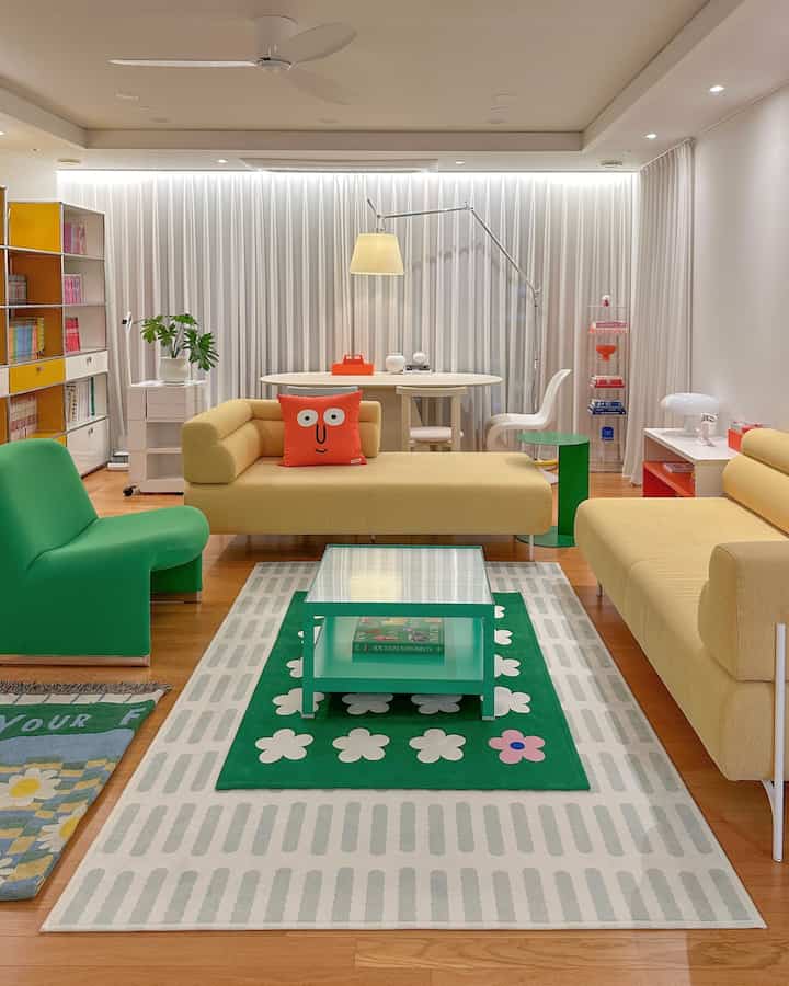 Bright modern living room featuring yellow sofas, green chair, and colorful rugs with a clean dining area in background