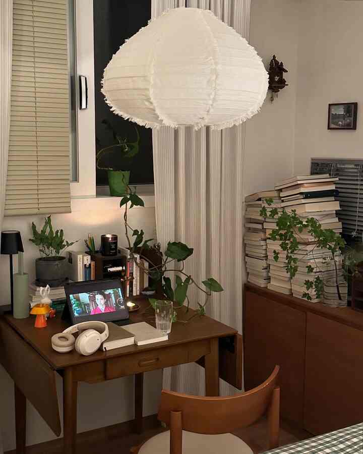 Natural-toned white-walled study featuring a wooden desk, cabinet filled with books and plants, creating a cozy atmosphere