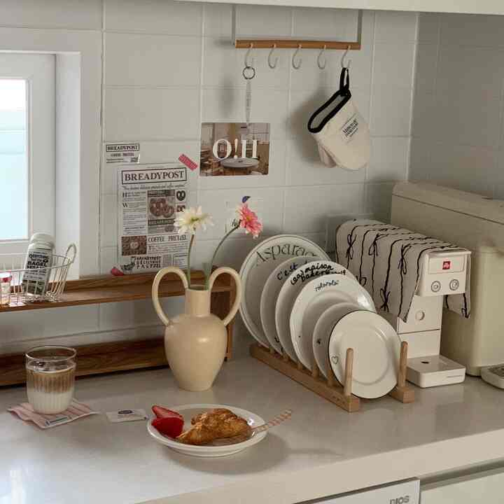 Cozy home cafe kitchen with white tiled walls, beige decorative vase, plate rack, and coffee machine