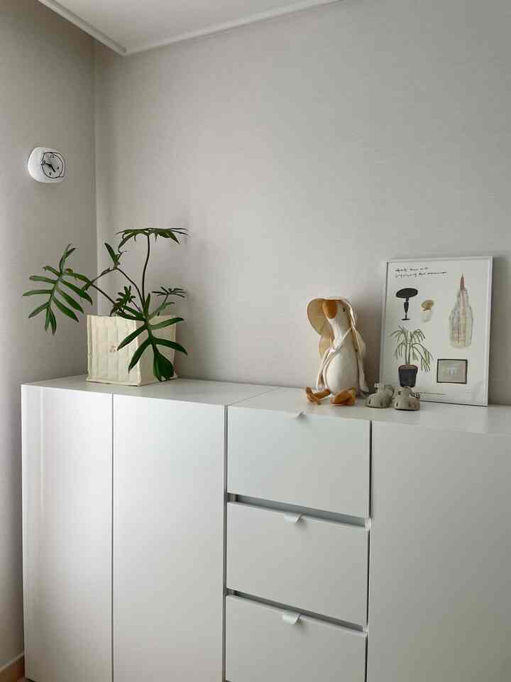 白を基調としたナチュラルトーンの空間、白い収納家具に植物と赤ちゃんの玩具が飾られたシンプルなインテリア