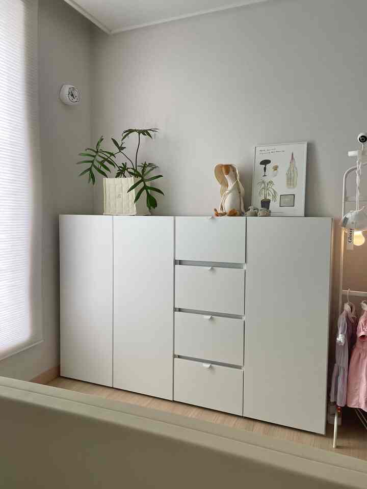 ホワイトとウッドトーンが調和した赤ちゃんの部屋、ホワイトの教具収納と小さなハンガーが配置された整った収納空間