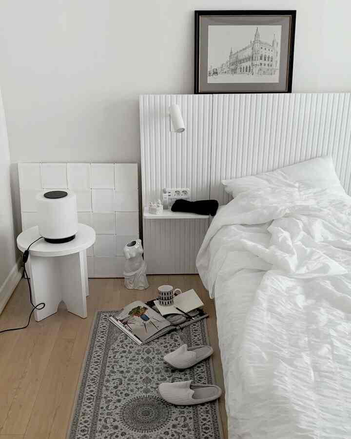White and gray toned bedroom featuring a white bed, rug, side table, and nightstand in a minimal and modern space