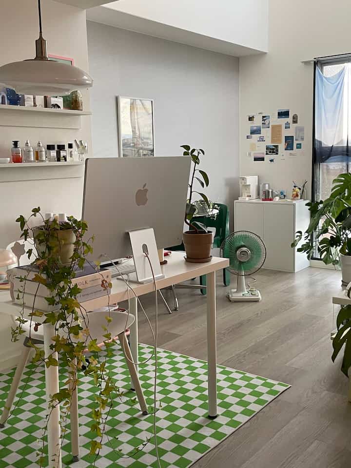 White and green toned studio apartment featuring desk, plants, and pendant light with a clean atmosphere