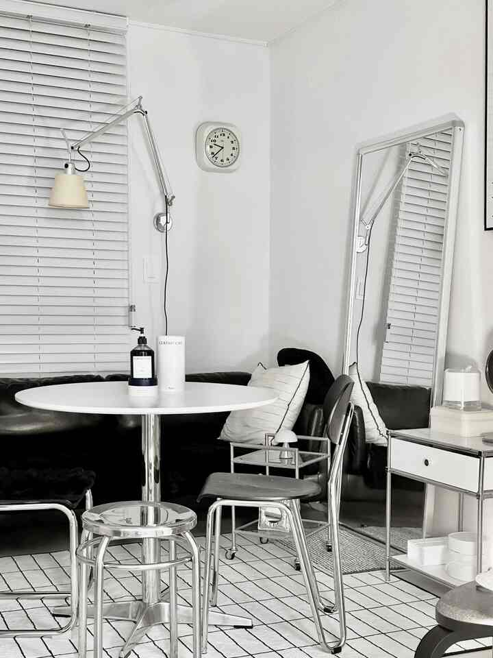 白い壁と黒いレザーソファがあるモノトーンの小さなリビング、アルミブラインドと全身鏡が配置されたモダンな空間