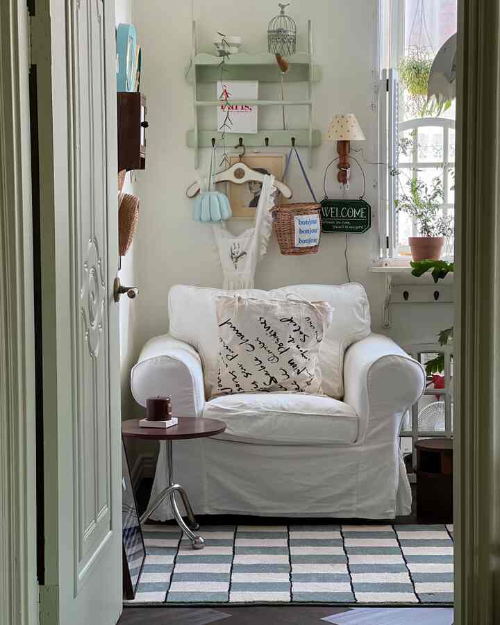 ホワイトとナチュラルカラーのベランダ窓がある居心地の良いリビング、中央にホワイトのアームチェアとチェック柄のラグが配置された空間