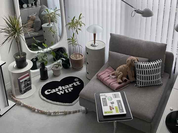 グレーとホワイトトーンの一人暮らしリビング、モダンなソファとサイドテーブル、大きな鏡と植物が配置されたシンプルな空間