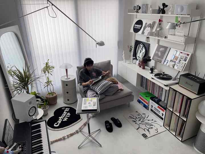 グレー調の一人暮らし向け音楽空間、1人用ソファとターンテーブル、本棚、フロアランプが配置されたモダンでミニマルなインテリア